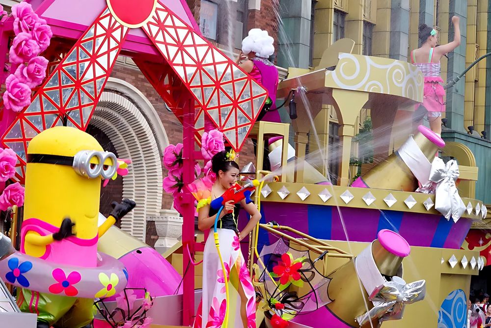 Parade float with a Minion and dancers in pink and floral costumes, USJ anniversary shows. Costume design by Cynthia Nordstrom
