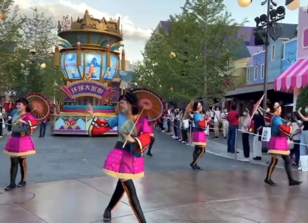 Dancers in pink skirts and black boots with parasols before a parade float, Universal Beijing parade. Costume design by Cynthia Nordstrom